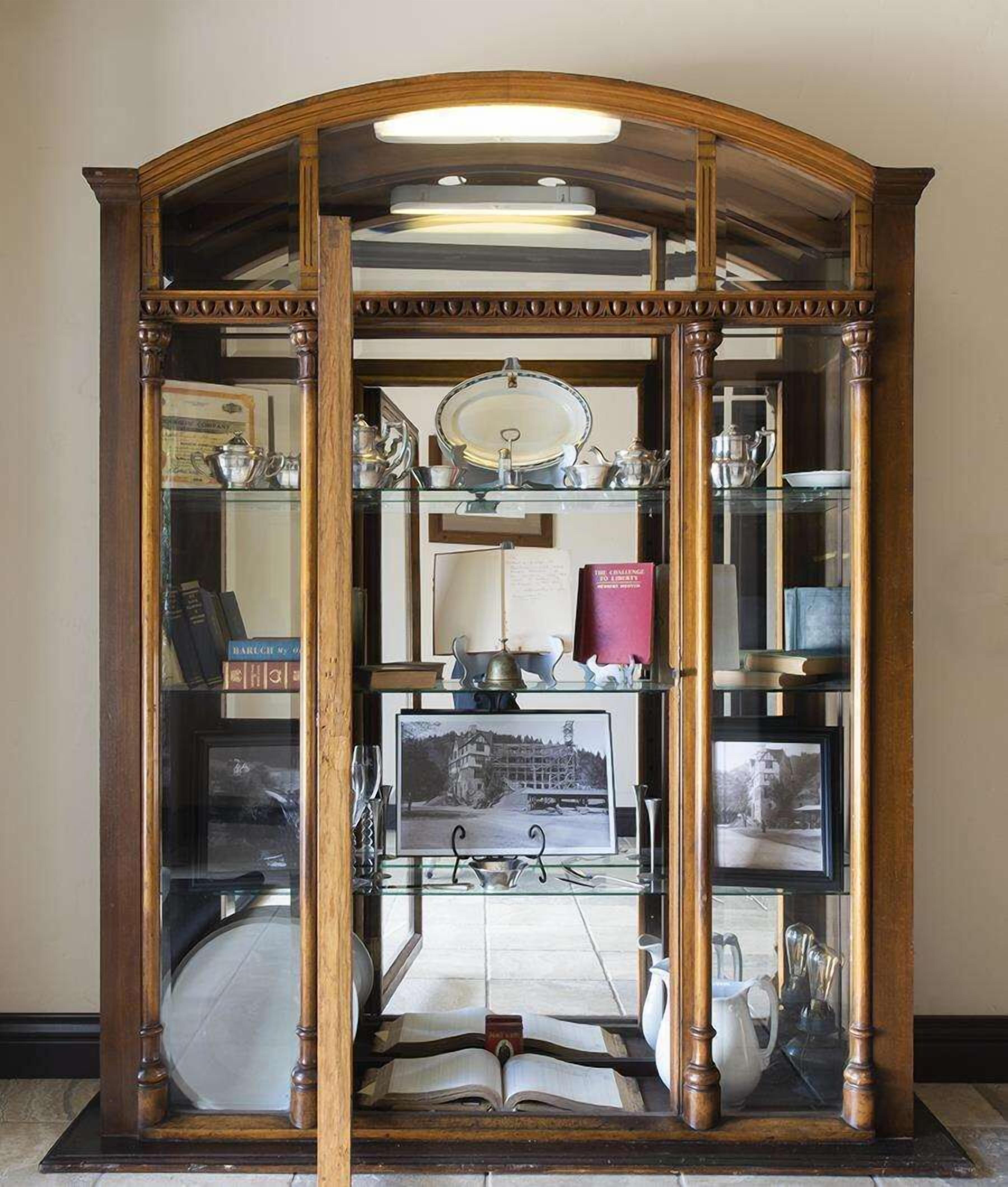 Un mueble de madera con puertas de cristal que contiene libros, una fotografía enmarco y objetos decorativos.