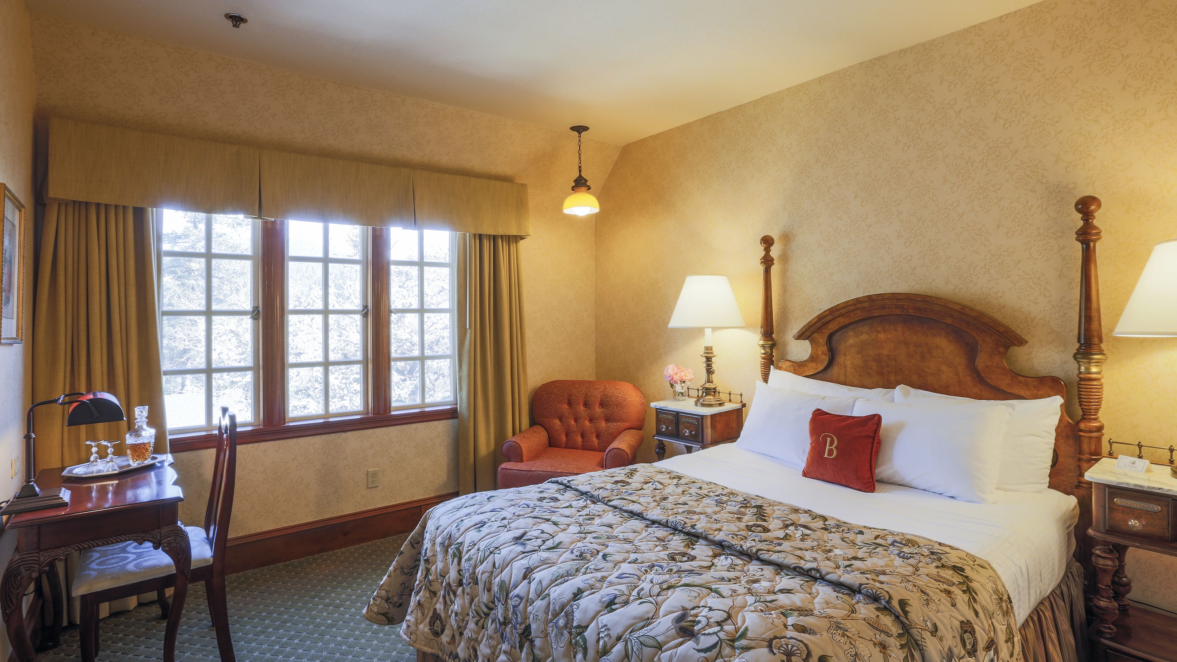 A hotel room with a large bed, a chair, a desk, and a window with curtains.