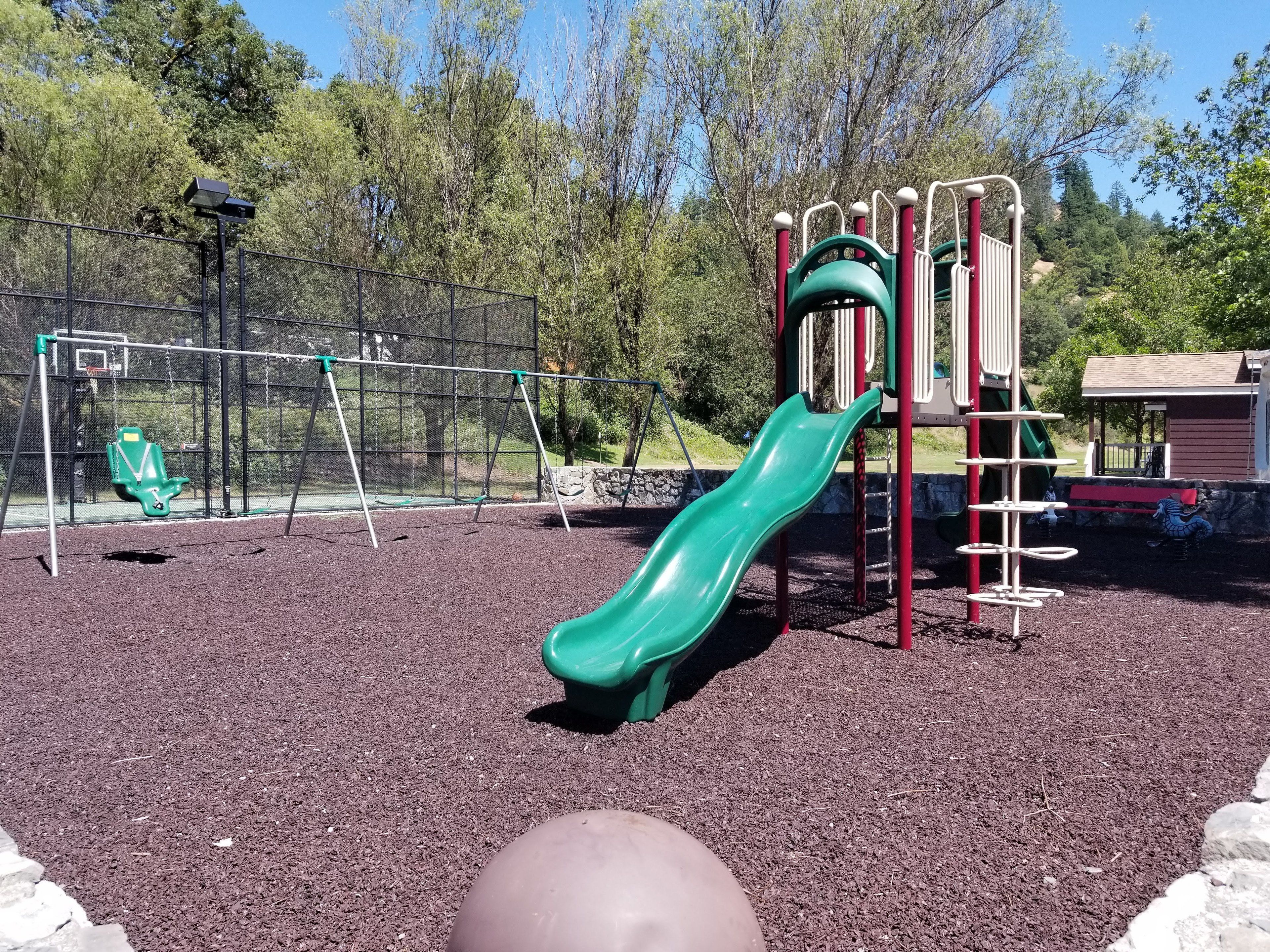 A playground with a green slide, swings, and a climbing structure.