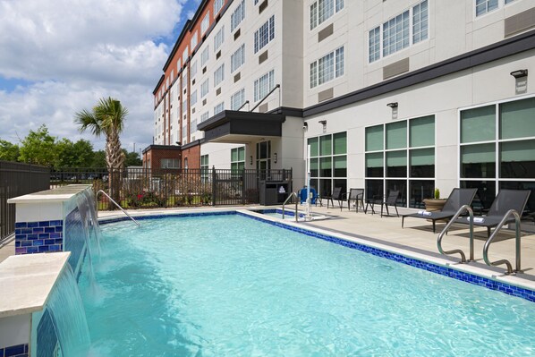 A swimming pool with lounge chairs and a building with multiple windows. - Four Points by Sheraton Houston West (Houston)