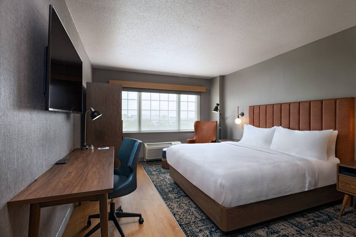 Une chambre d’hôtel avec un lit, un bureau, une chaise, une télévision et une fenêtre.