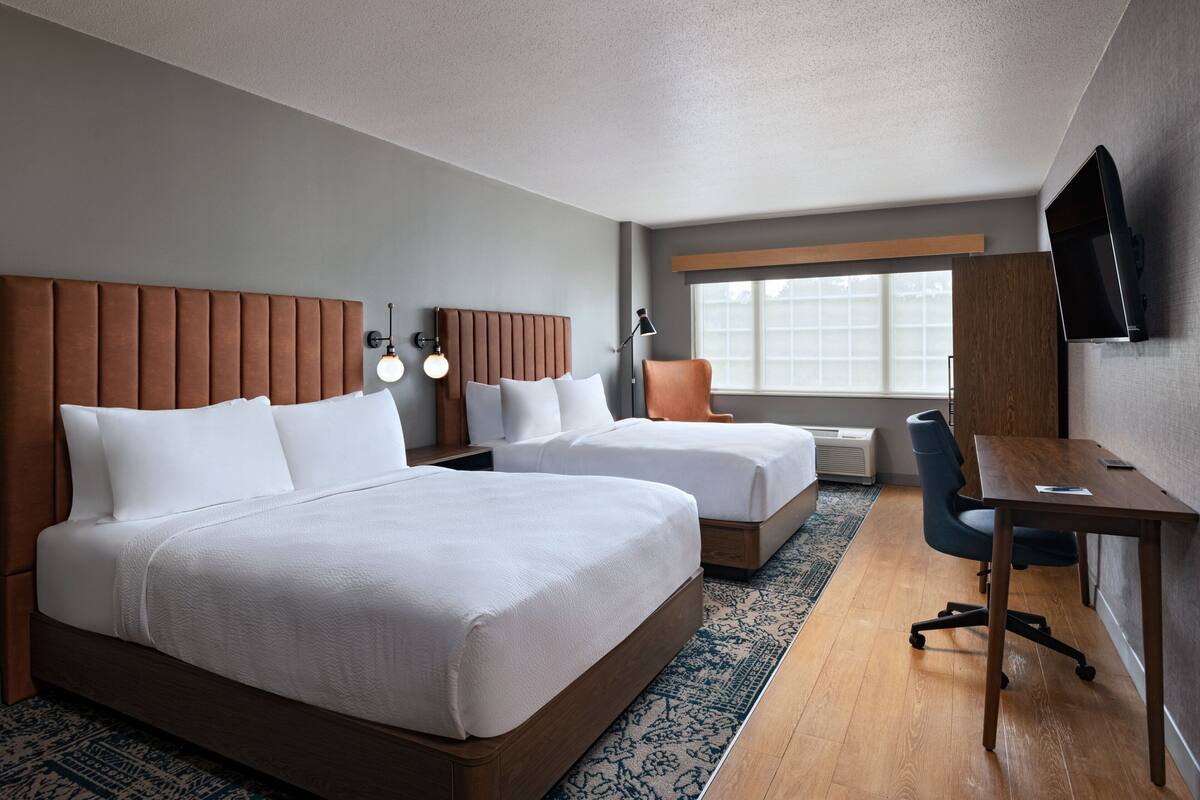 Une chambre d’hôtel avec deux lits, un bureau, une chaise, une télévision et une fenêtre.