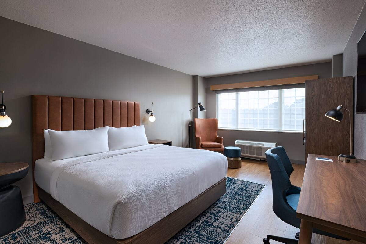 Une chambre d’hôtel moderne, dotée d’un grand lit, d’un bureau, d’une chaise et d’une fenêtre offrant une vue agréable.