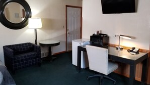 Ett hotellrum med ett skrivbord, en stol, en tv och en rund spegel.