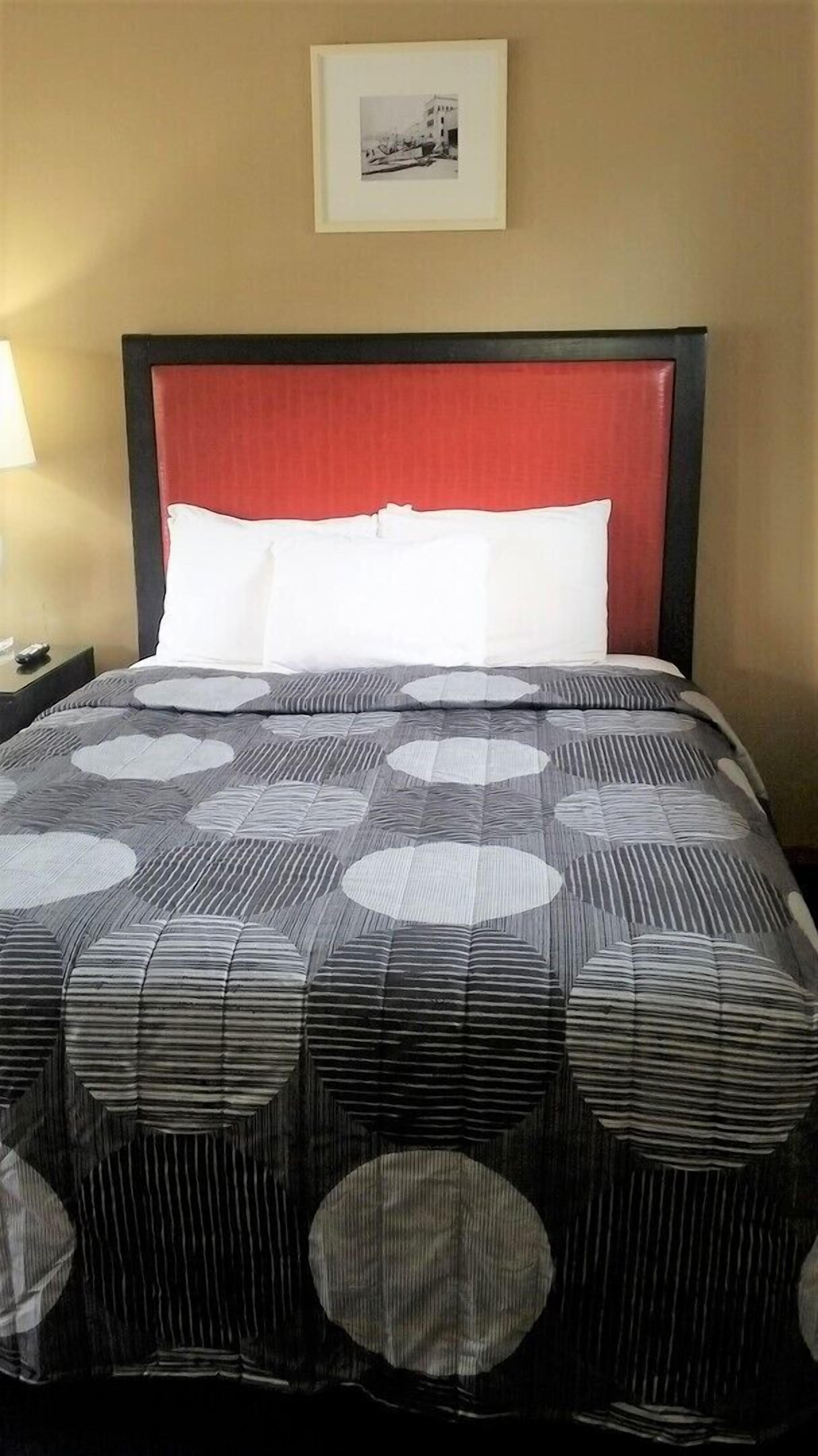 Una habitación de hotel con una cama, una mesita de noche, una lámpara y un cuadro en la pared.