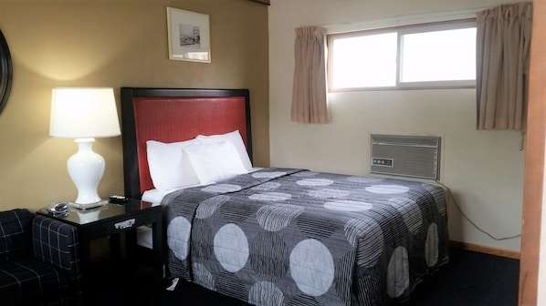 Habitación de hotel con cama, escritorio con lámpara, silla, un cuadro en la pared y ventana con cortinas.