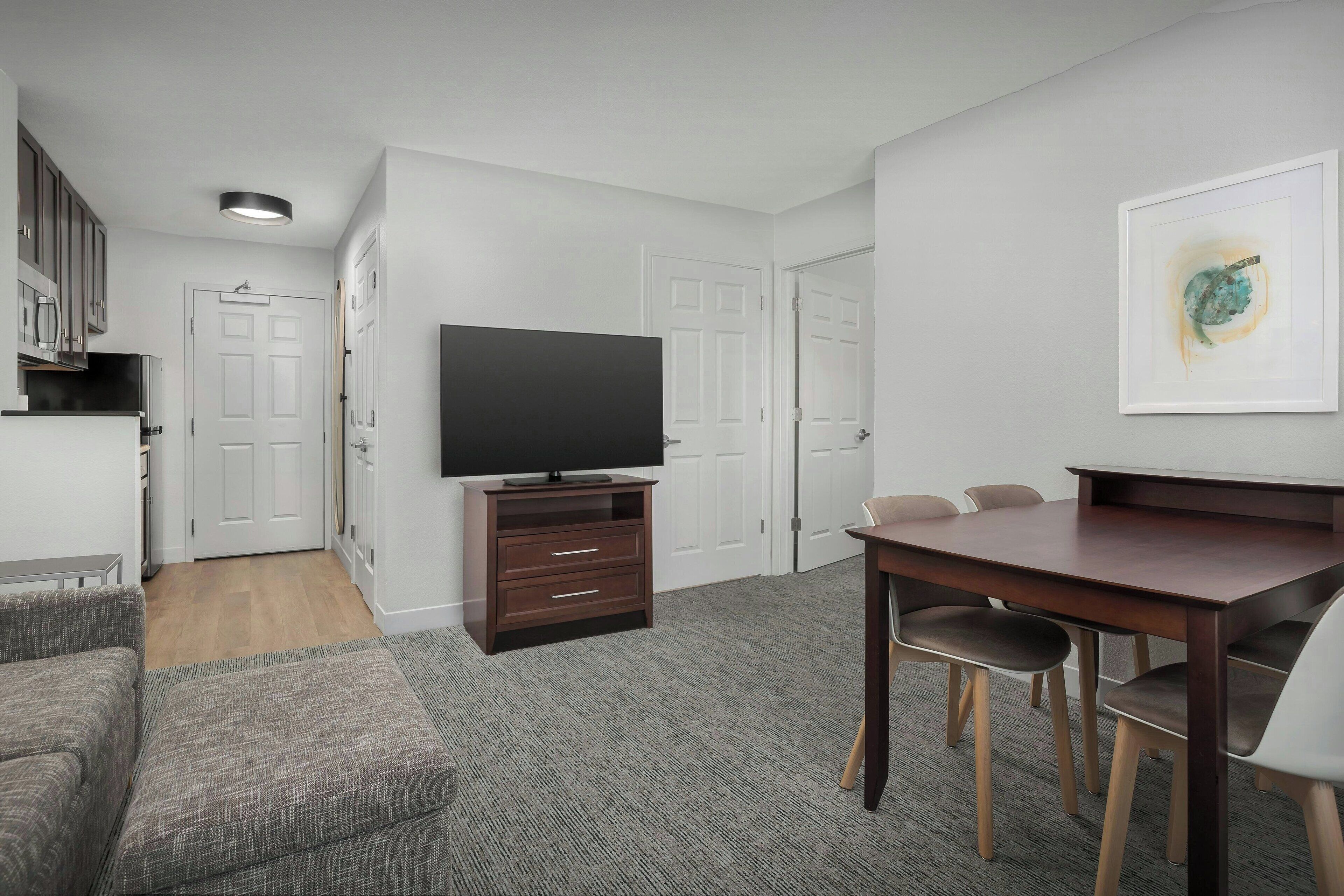 Una sala de estar moderna con una televisión de pantalla plana, una mesa de comedor con sillas, un sofá y suelo cubierto de alfombra.