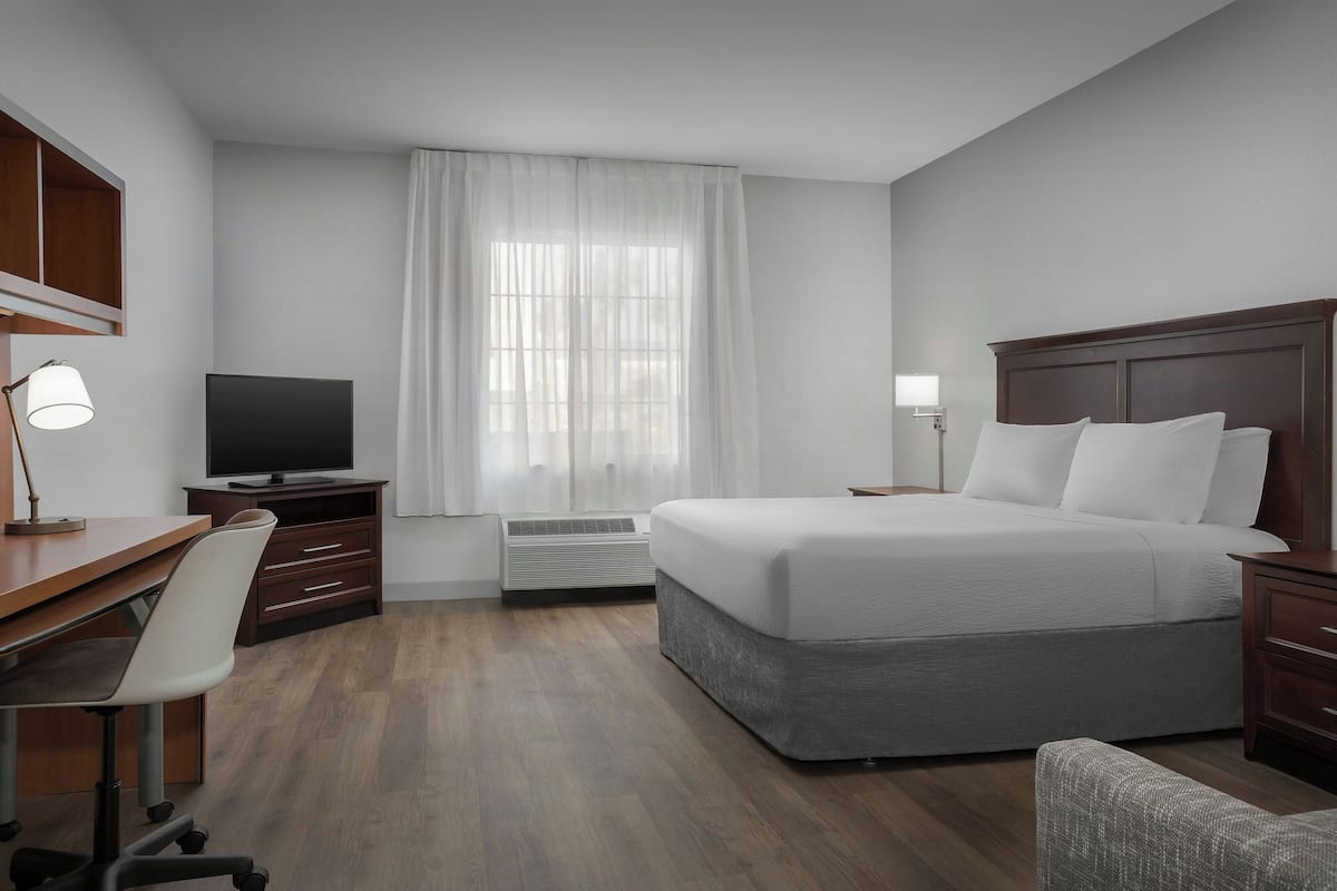 A hotel room with a bed, desk, chair, TV, and a window with curtains.