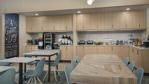 A modern kitchen with wooden cabinets, a dining area with a large table and chairs, and a breakfast sign on the wall. - TownePlace Suites Marriott El Centro (El Centro)
