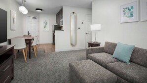 A modern living room with a grey sofa, a dining table with chairs, a TV, and a kitchen area in the background. - TownePlace Suites Marriott El Centro (El Centro)