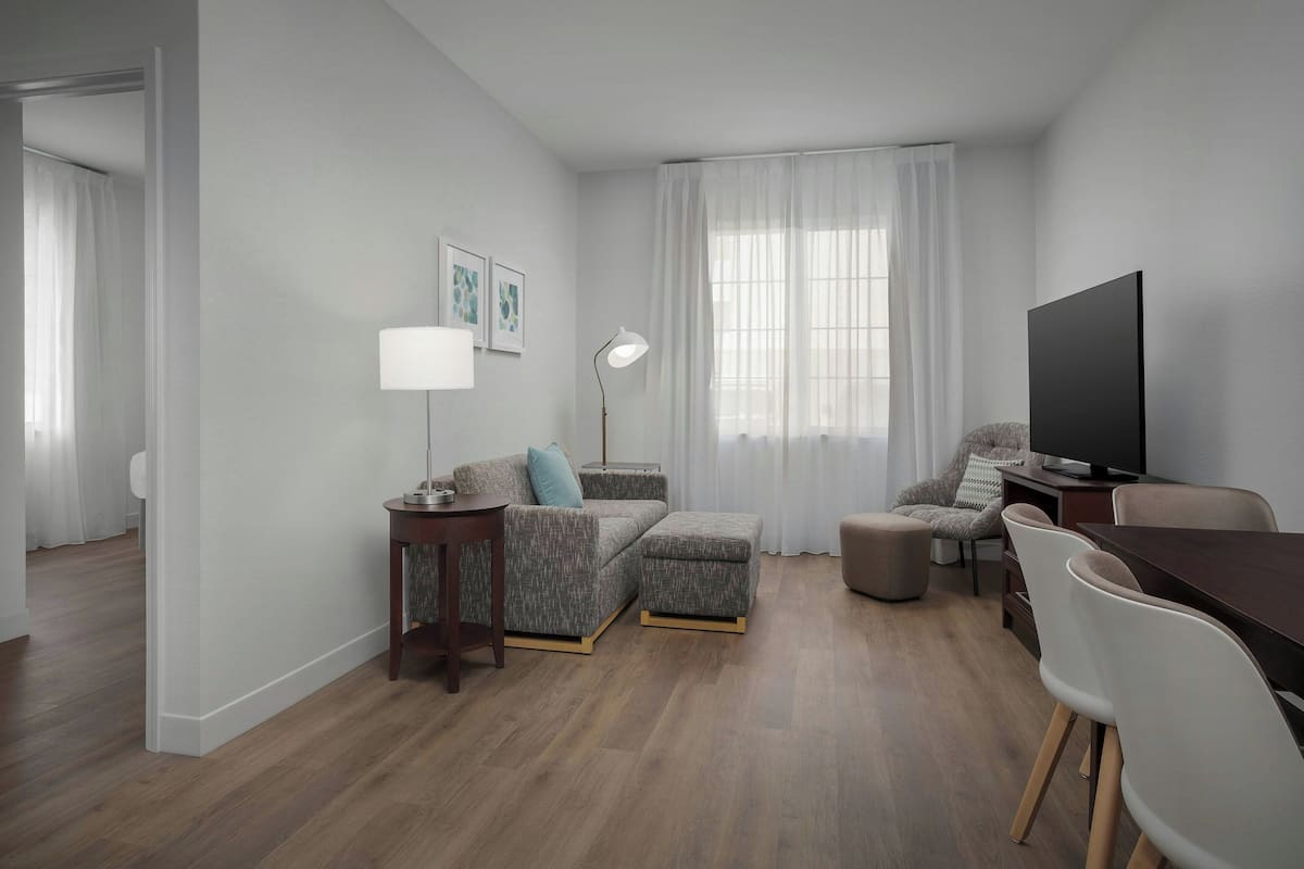 A modern living room with a sofa, ottoman, TV, and dining area.