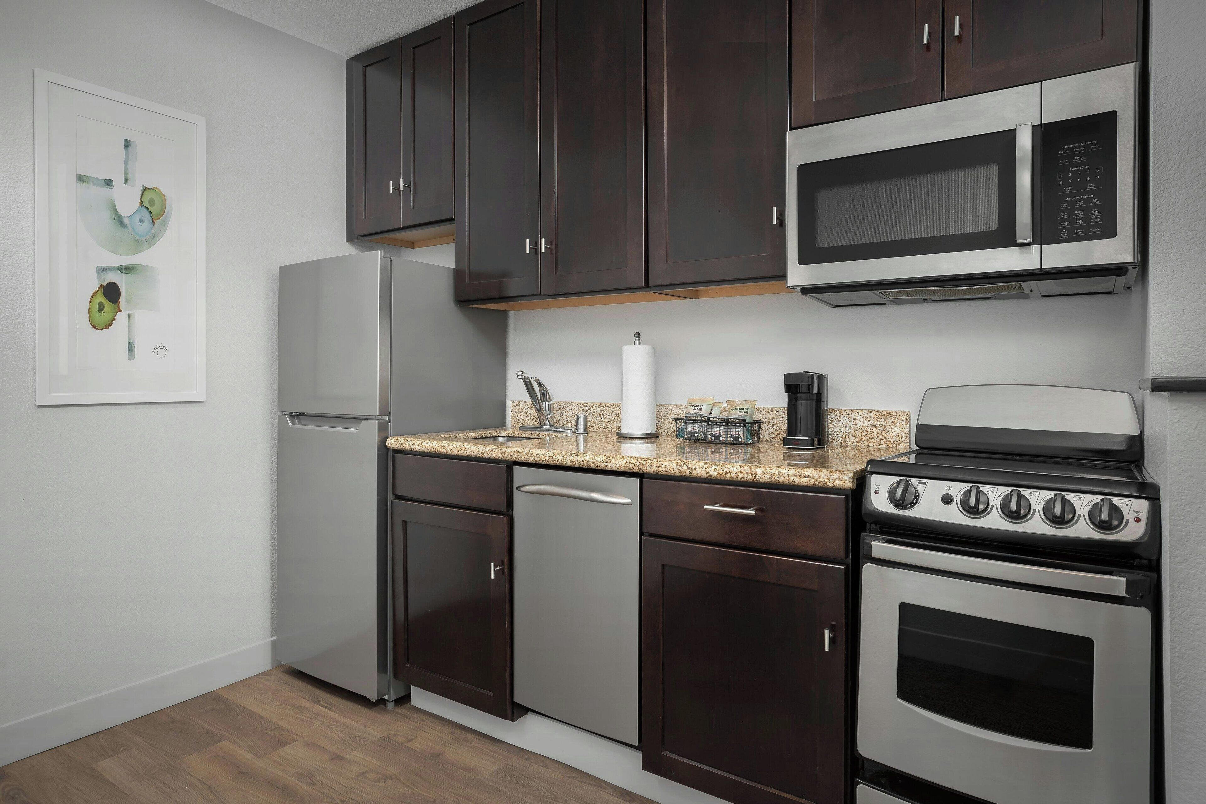 A modern kitchen with dark wood cabinets, stainless steel appliances including a refrigerator, dishwasher, microwave, and stove.