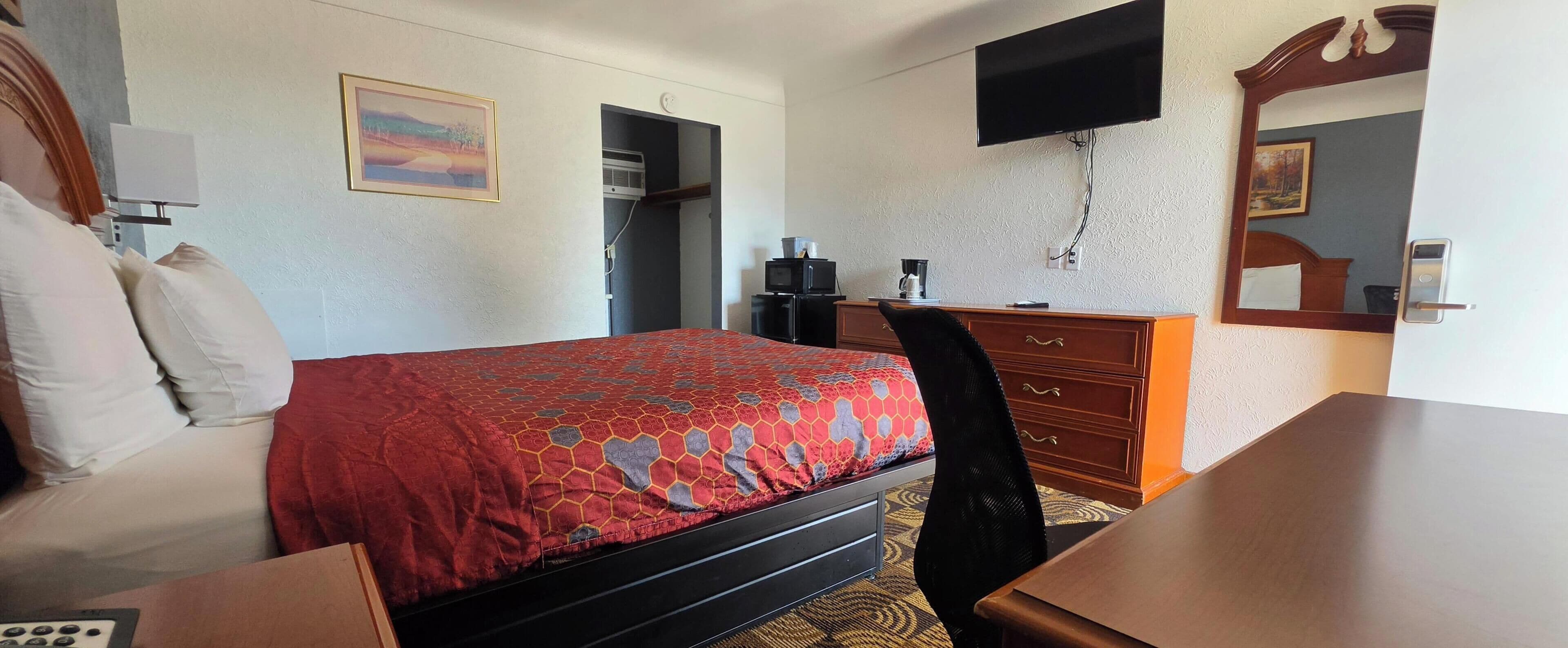 A hotel room with a bed, a desk, a chair, a dresser, a television, and a painting on the wall.