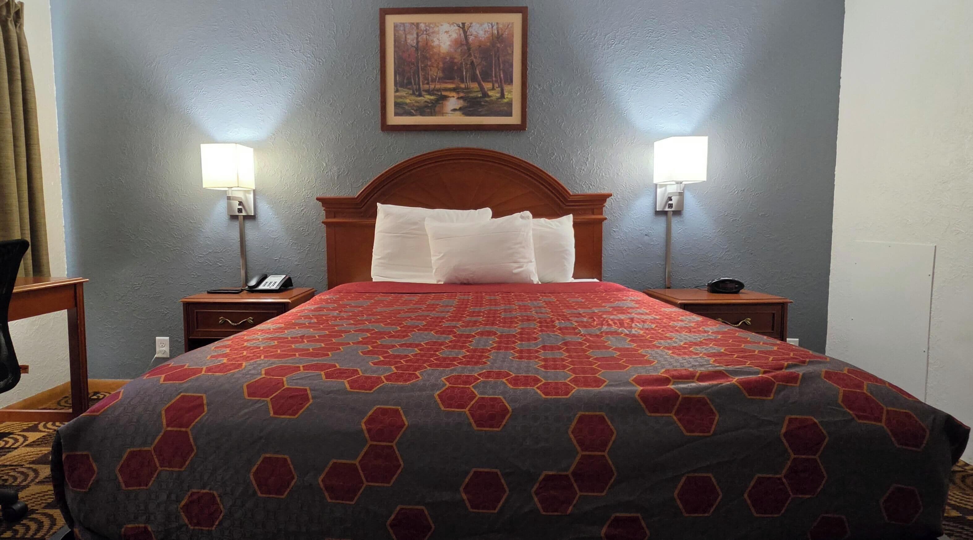 Habitación de hotel con una cama grande, dos mesitas de noche con lámparas, un cuadro en la pared y piso alfombrado.
