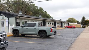Un estacionamiento con una camioneta azul claro y un sedán rojo aparcados frente a un motel con aviso de piscina.