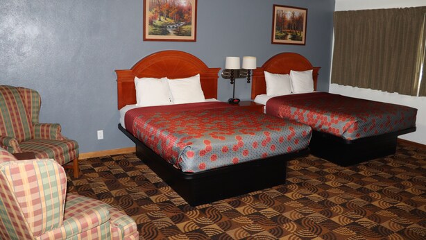 A hotel room with two beds, a chair, and two paintings on the wall.
