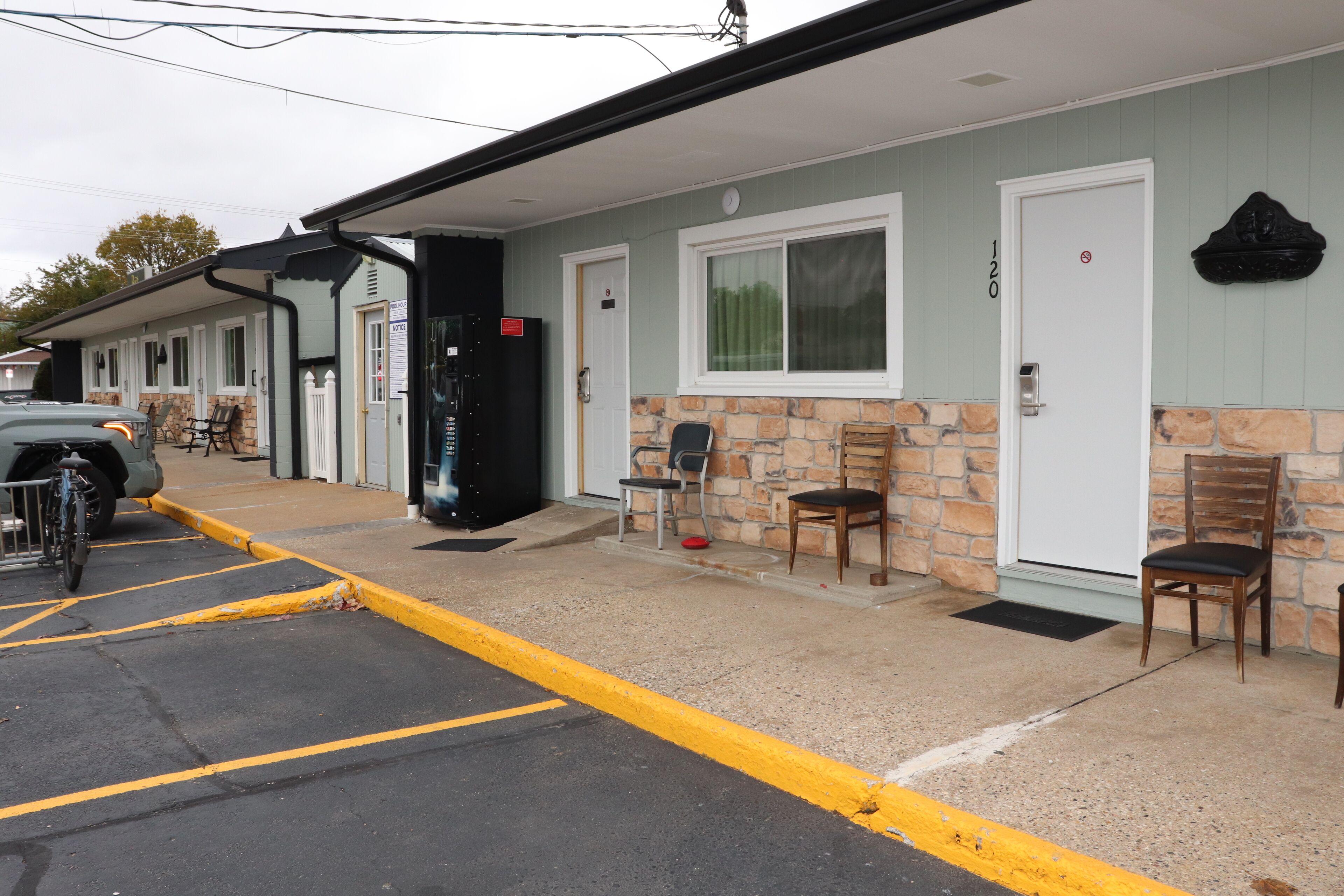 A motel with a parking lot, a covered outdoor seating area, and a stone facade.
