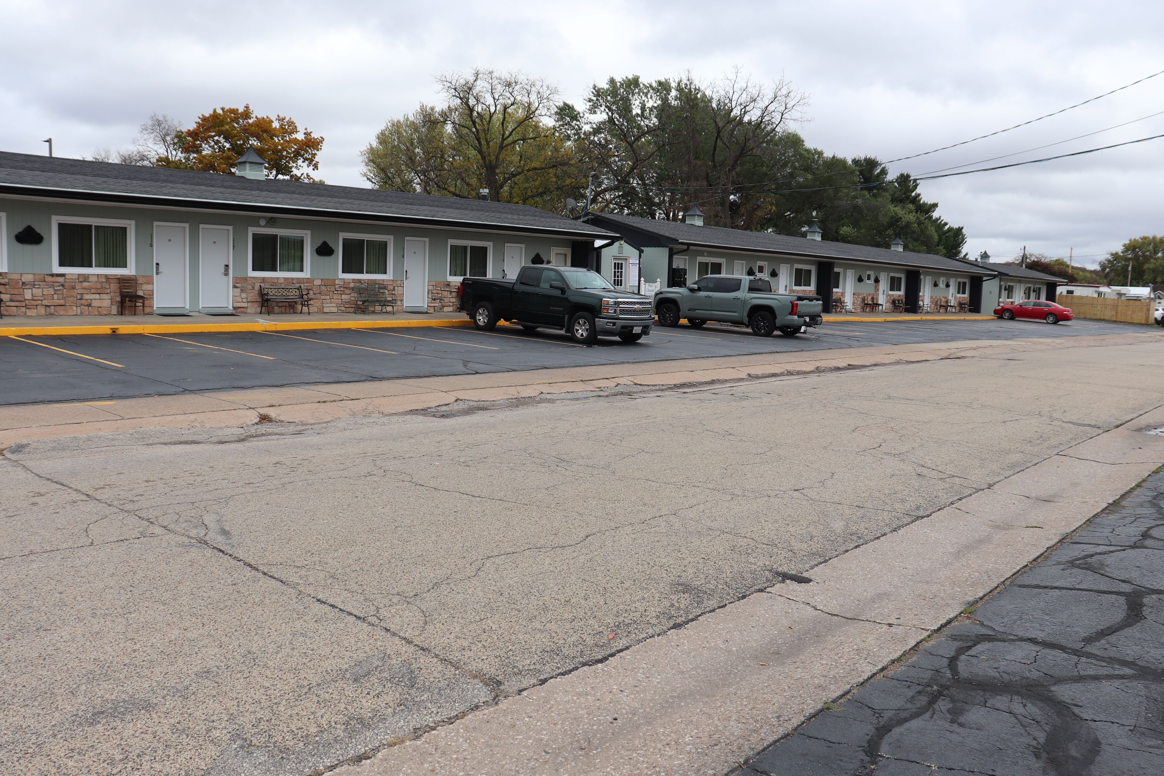 A motel with a row of rooms, a parking lot, and a few parked vehicles.