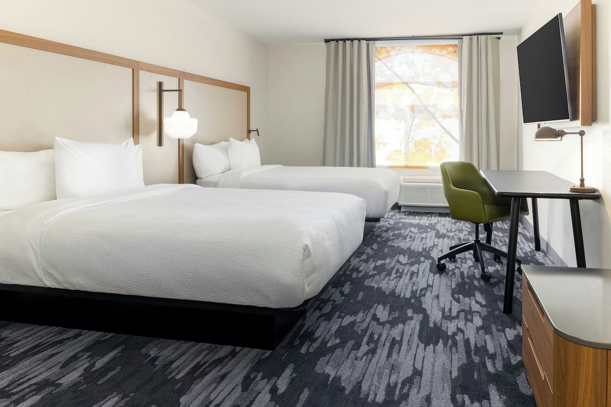 A hotel room with two beds, a desk, a chair, a TV, and a window with curtains.