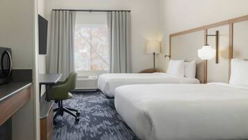 A hotel room with two beds, a desk, a chair, a lamp, and a window with curtains.