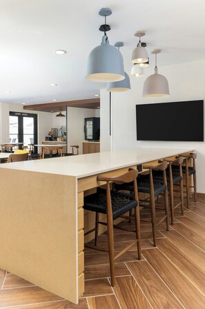Une cuisine moderne dotée d’un îlot central, de luminaires suspendus et d’un téléviseur à écran plat fixé au mur.