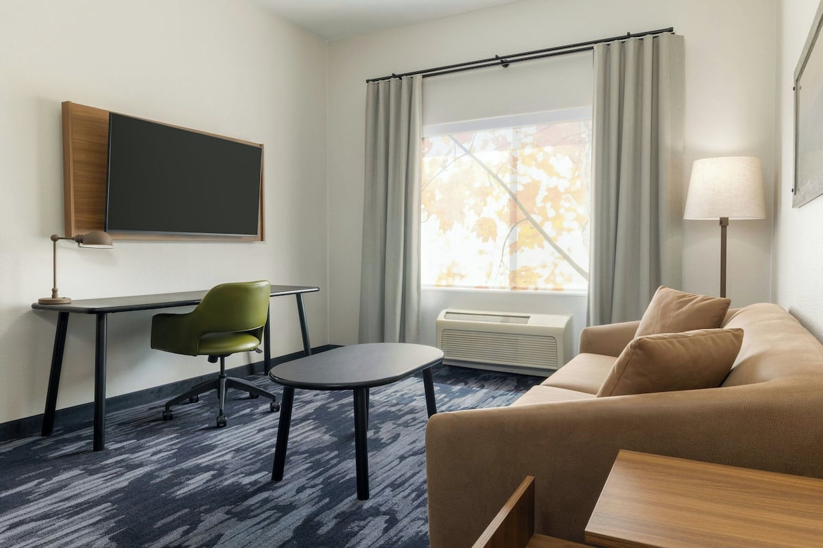 A hotel room with a desk, chair, couch, and a large window with curtains.