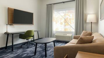 A hotel room with a desk, chair, couch, and a large window with curtains.