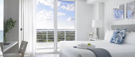 Une chambre d’hôtel moderne dotée d’un grand lit, d’un bureau et offrant une vue sur les toits de la ville grâce à de grandes fenêtres du sol au plafond.