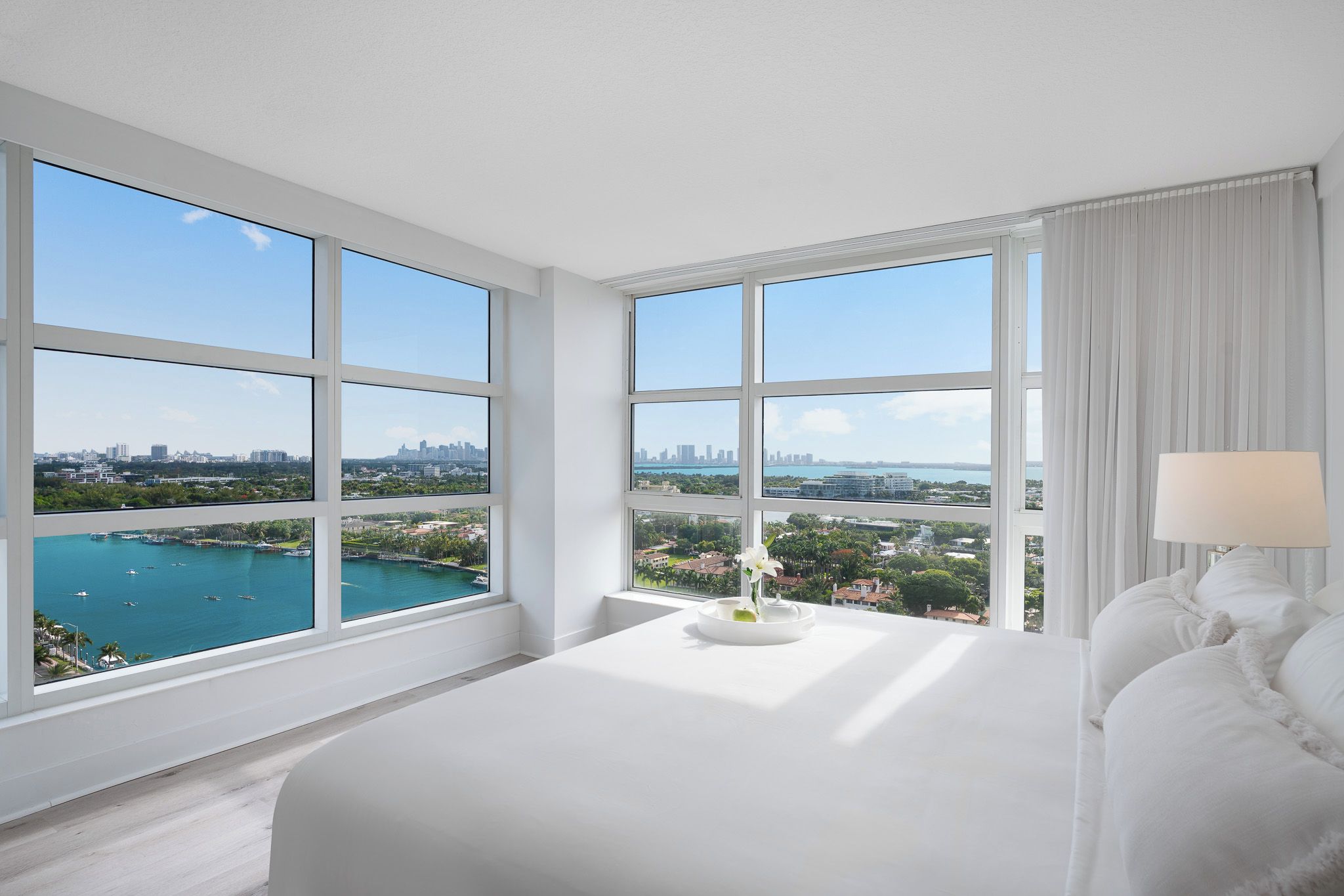 A hotel room with large windows, a bed, a bedside table, and a lamp.