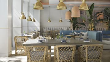 Un comedor con sillas de mimbre, una mesa de madera y lámparas colgantes doradas.