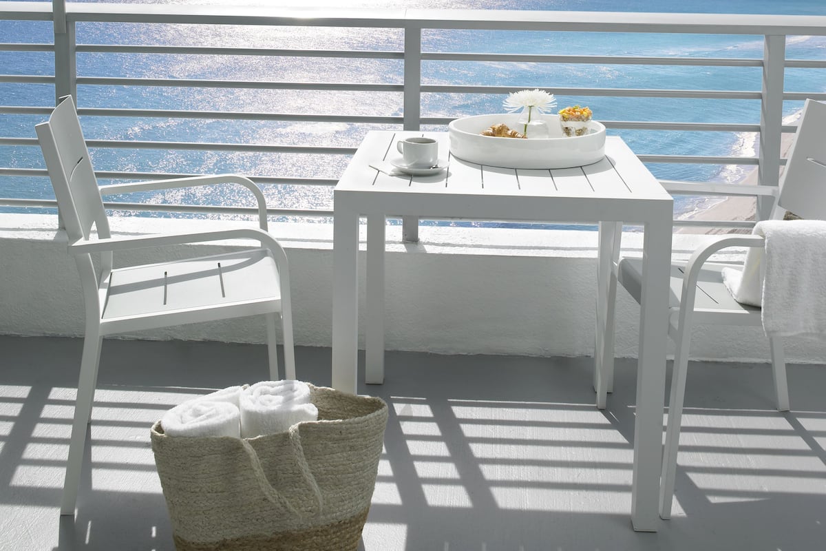 A white table with chairs and a basket on a balcony overlooking the sea.