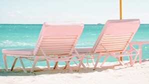 Two pink beach chairs and a pink umbrella on a sandy beach with a clear blue sky. - Grand Beach Hotel (Miami Beach)