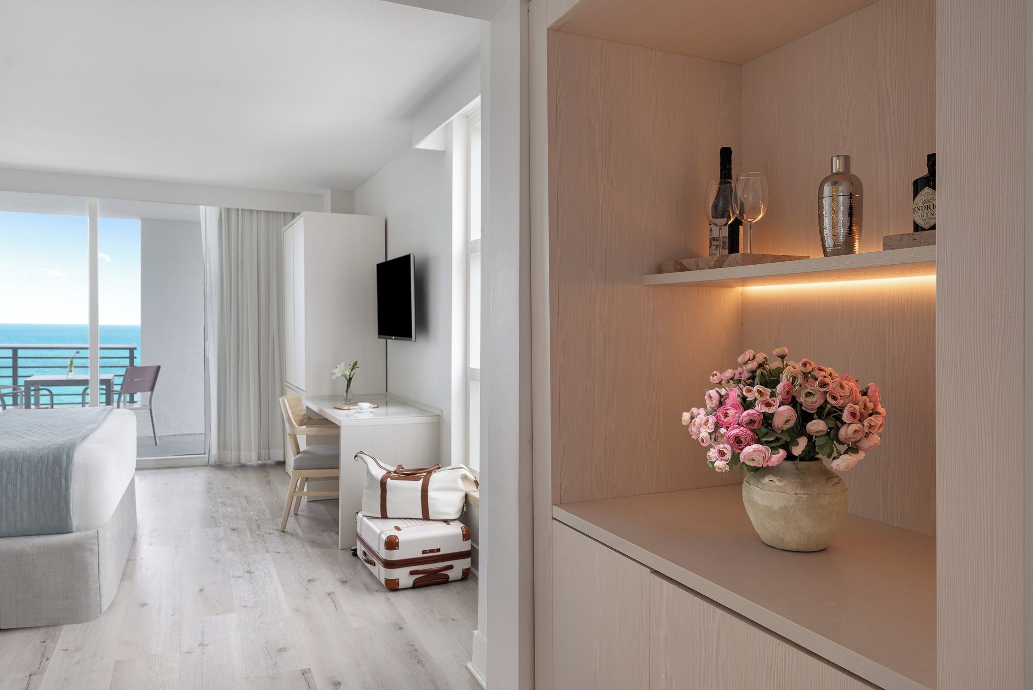 Ein modernes Hotelzimmer mit Balkon, Schreibtisch, Fernseher und einer Ablage mit Flaschen.