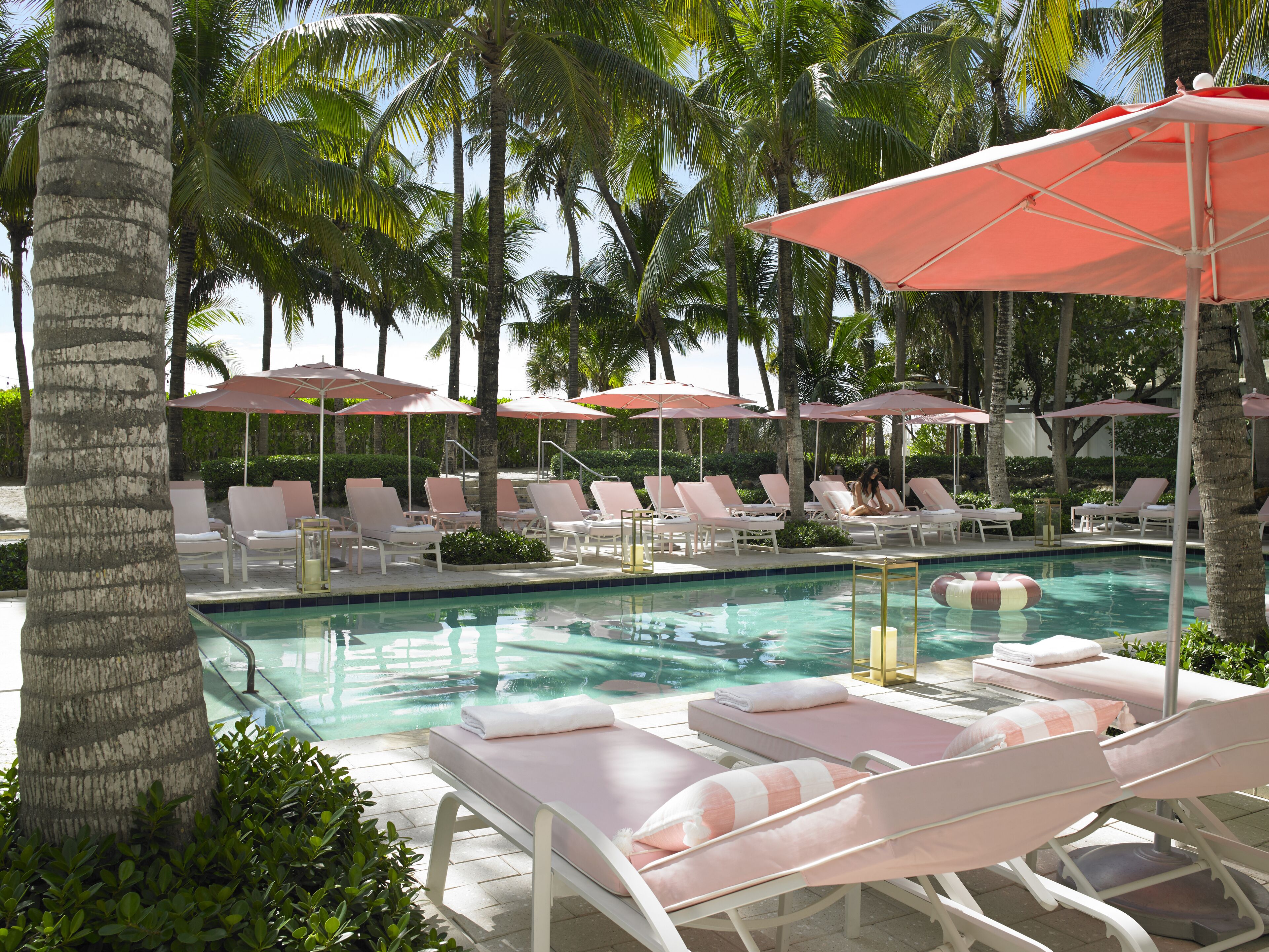 A poolside area with lounge chairs and umbrellas, surrounded by palm trees.