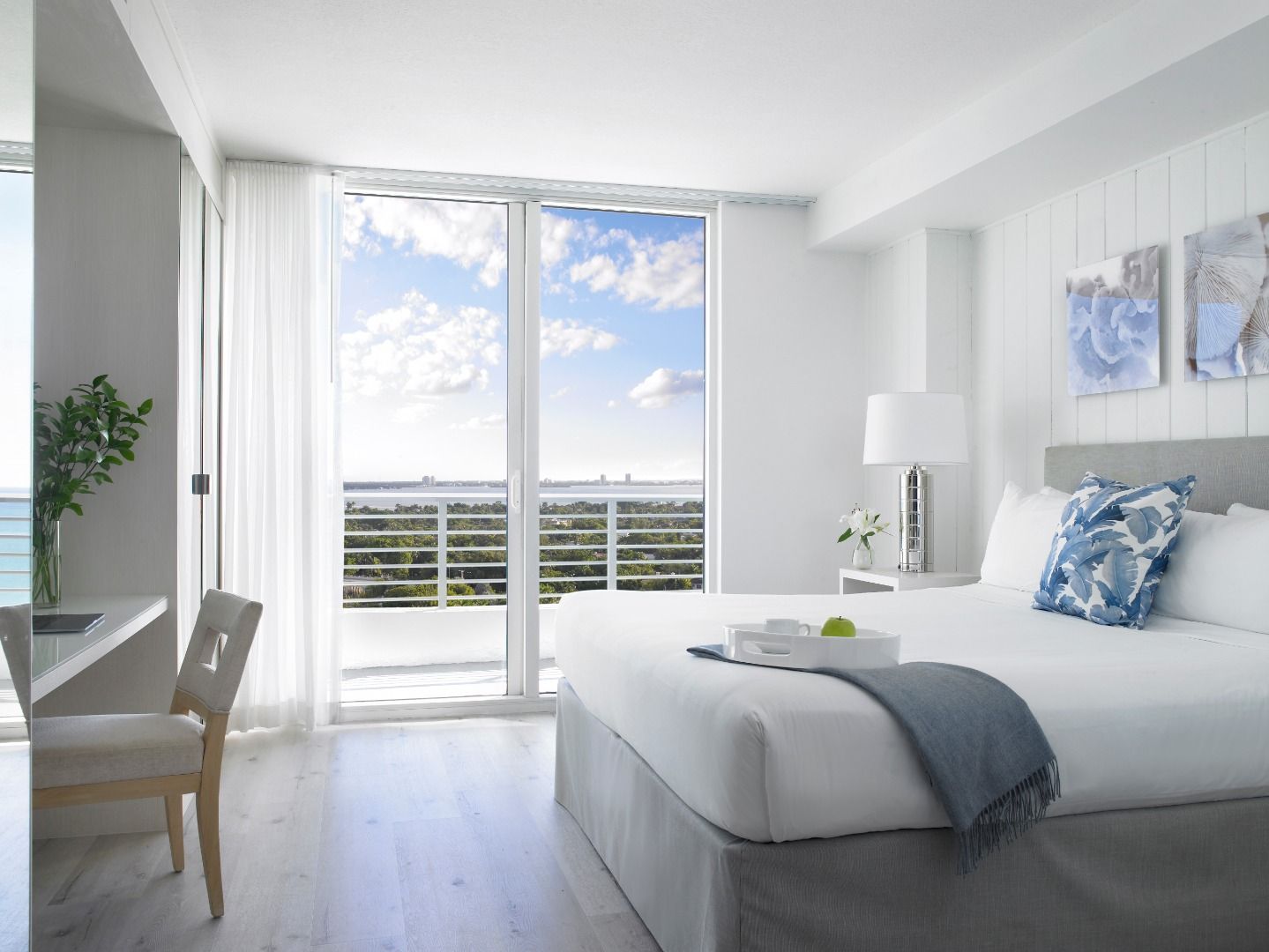Une chambre d’hôtel moderne dotée d’un grand lit, d’un bureau et offrant une vue sur le paysage urbain grâce à de grandes fenêtres du sol au plafond.