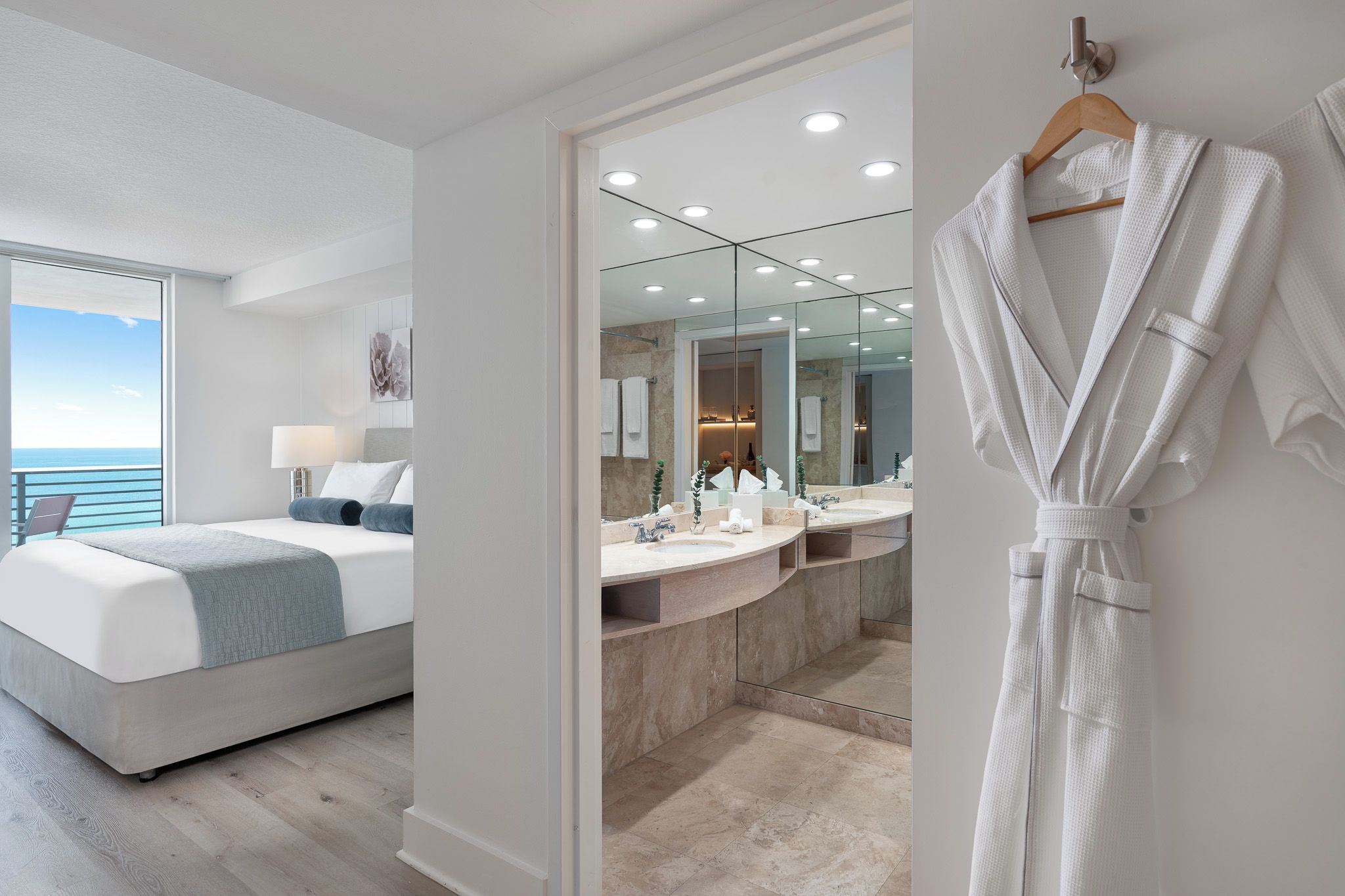 A modern bedroom with a large bed, a bathroom with a vanity and mirror, and a view of the sea.