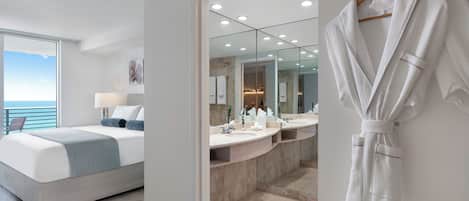 A modern bedroom with a large bed, a bathroom with a vanity and mirror, and a view of the sea.