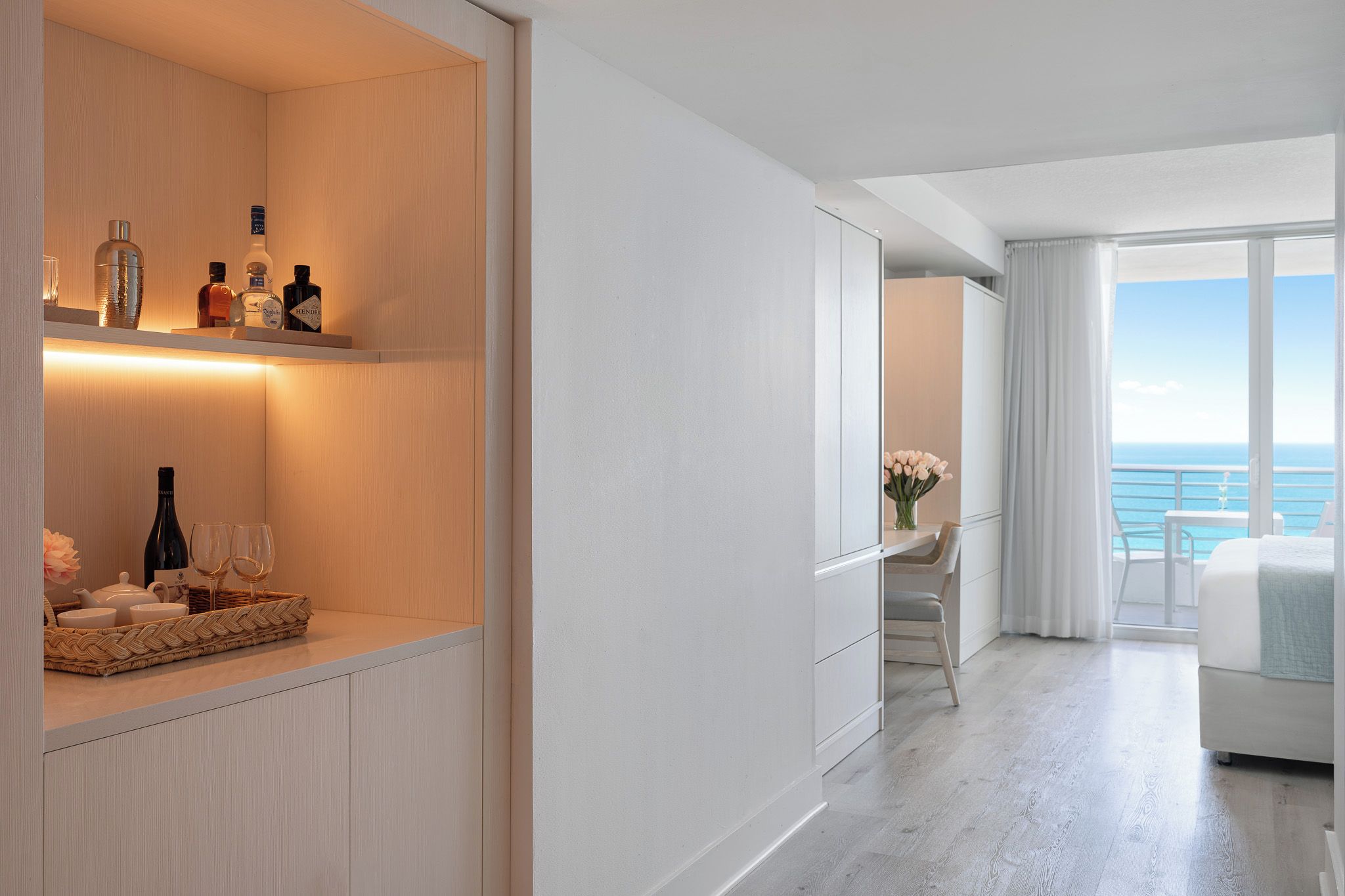 A modern hotel room with a balcony, a minibar, and a view of the sea.