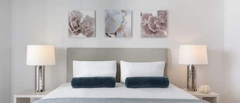 Una cama bien hecha con dos almohadas, un edredón gris y dos lámparas de noche a cada lado.
