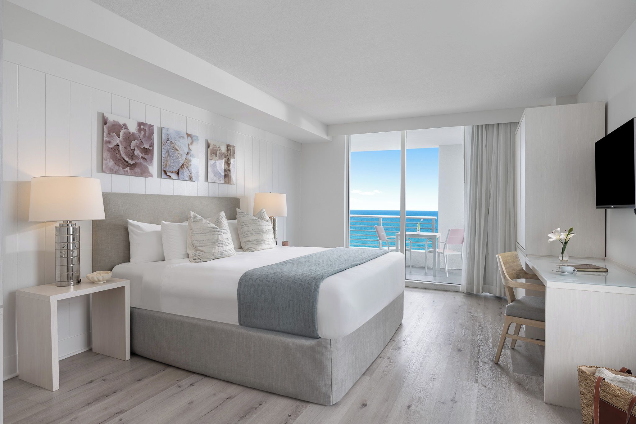 A modern hotel room with a large bed, a desk, and a view of the ocean.