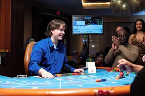 A casino table with chips and cards, a monitor displaying game results, and a person seated at the table.