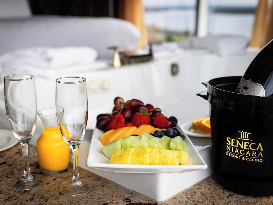 A breakfast setting with a fruit platter, two glasses, a juice, and a hot chocolate bucket labeled "Seneca Niagara Resort & Casino".