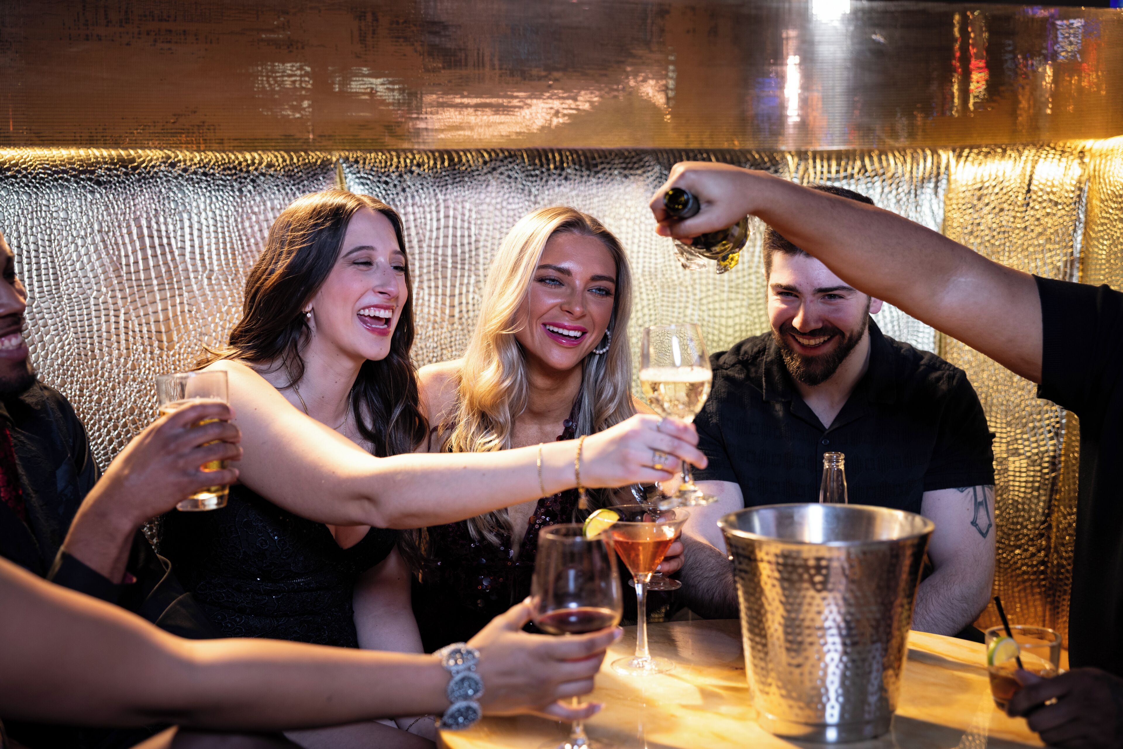 Eine Gruppe von Personen sticht mit Getränken in einer Bar an, deren Wand eine strukturierte Oberfläche hat.