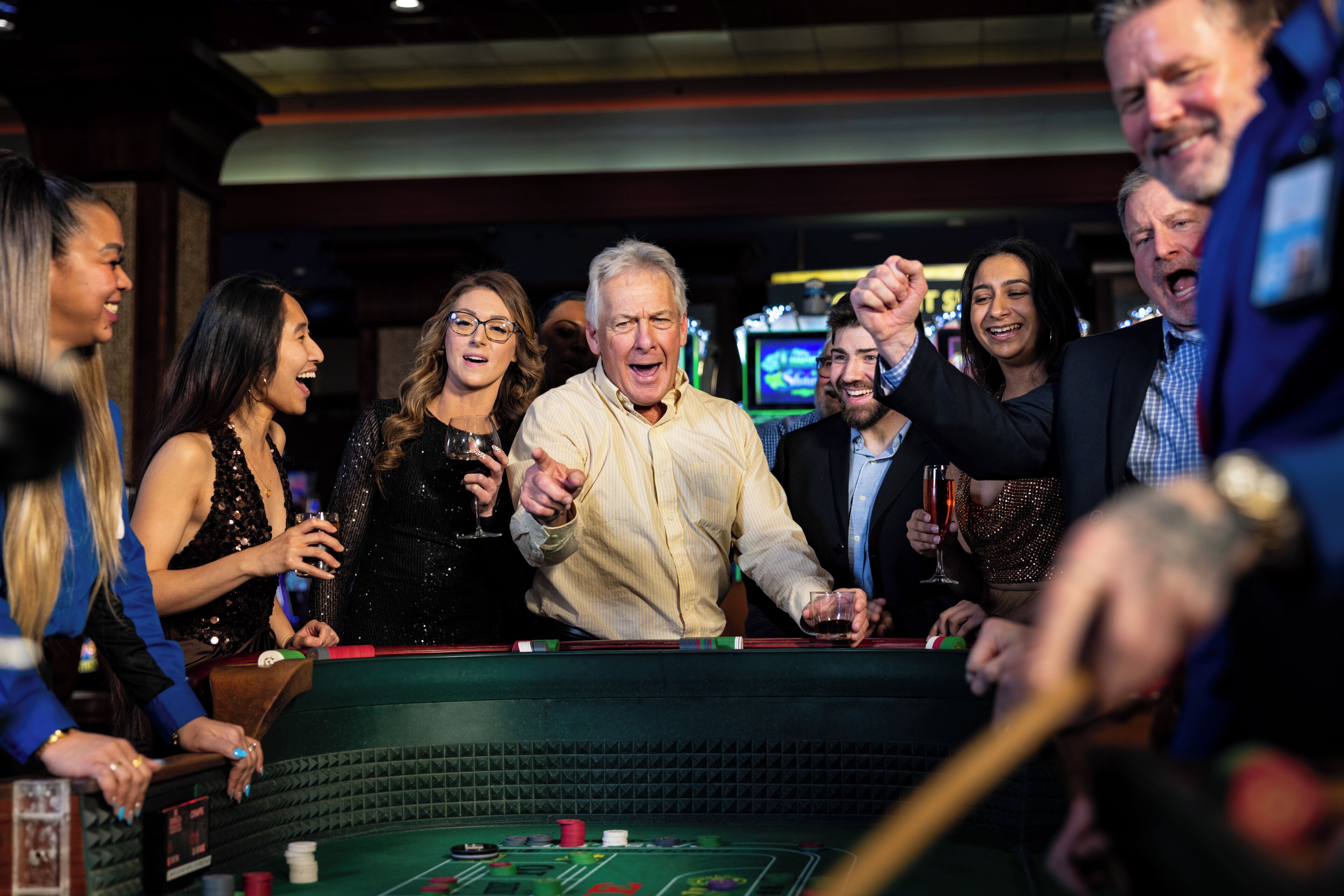 Un groupe de personnes est assis autour d’une table de casino, dont le plateau est recouvert d’un feutre vert. Ils jouent aux cartes et misent des jetons.
