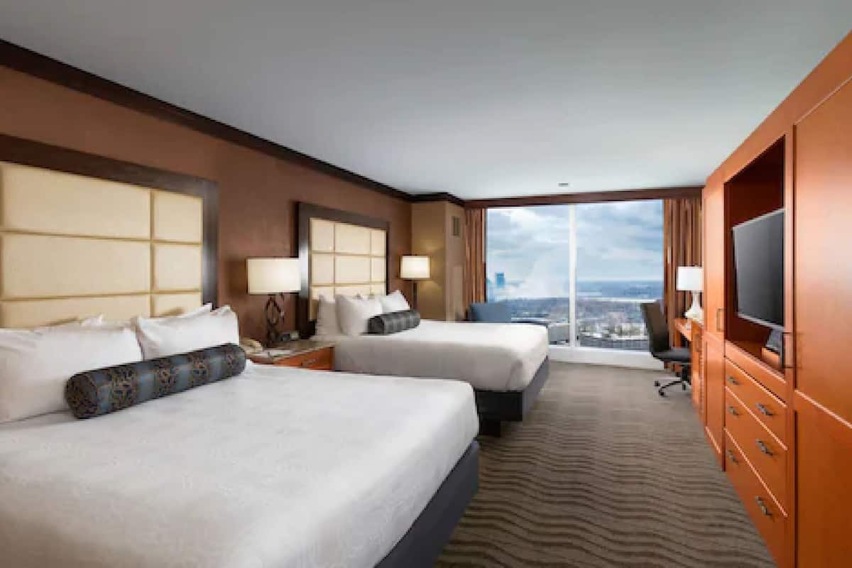 Habitación de hotel con dos camas, televisión y vista a la ciudad.