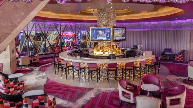 Een bar met een ronde toog, diverse zithoeken en een groot scherm waarop iets wordt vertoond.