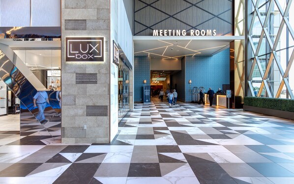 Un hall d’hôtel avec un sol à carreaux, une enseigne « LUX box » et une autre indiquant « SALLES DE RÉUNION ».