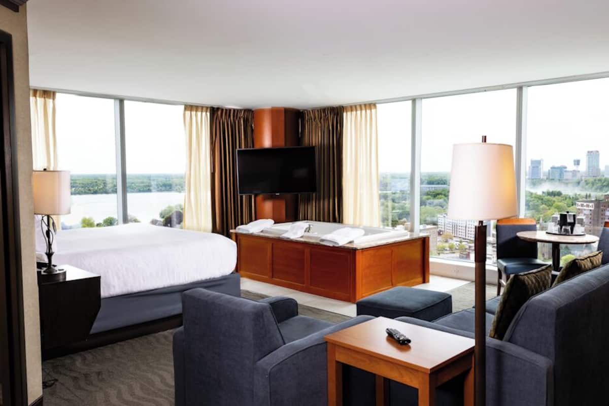 Habitación de hotel con una cama grande, un sofá, un televisor y vistas a un paisaje urbano.