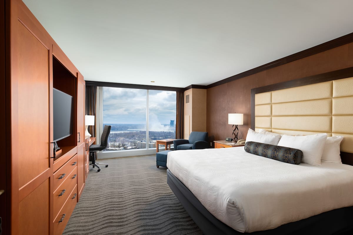 Habitación de hotel con una cama grande, un escritorio, una silla, un televisor y vistas a la ciudad.