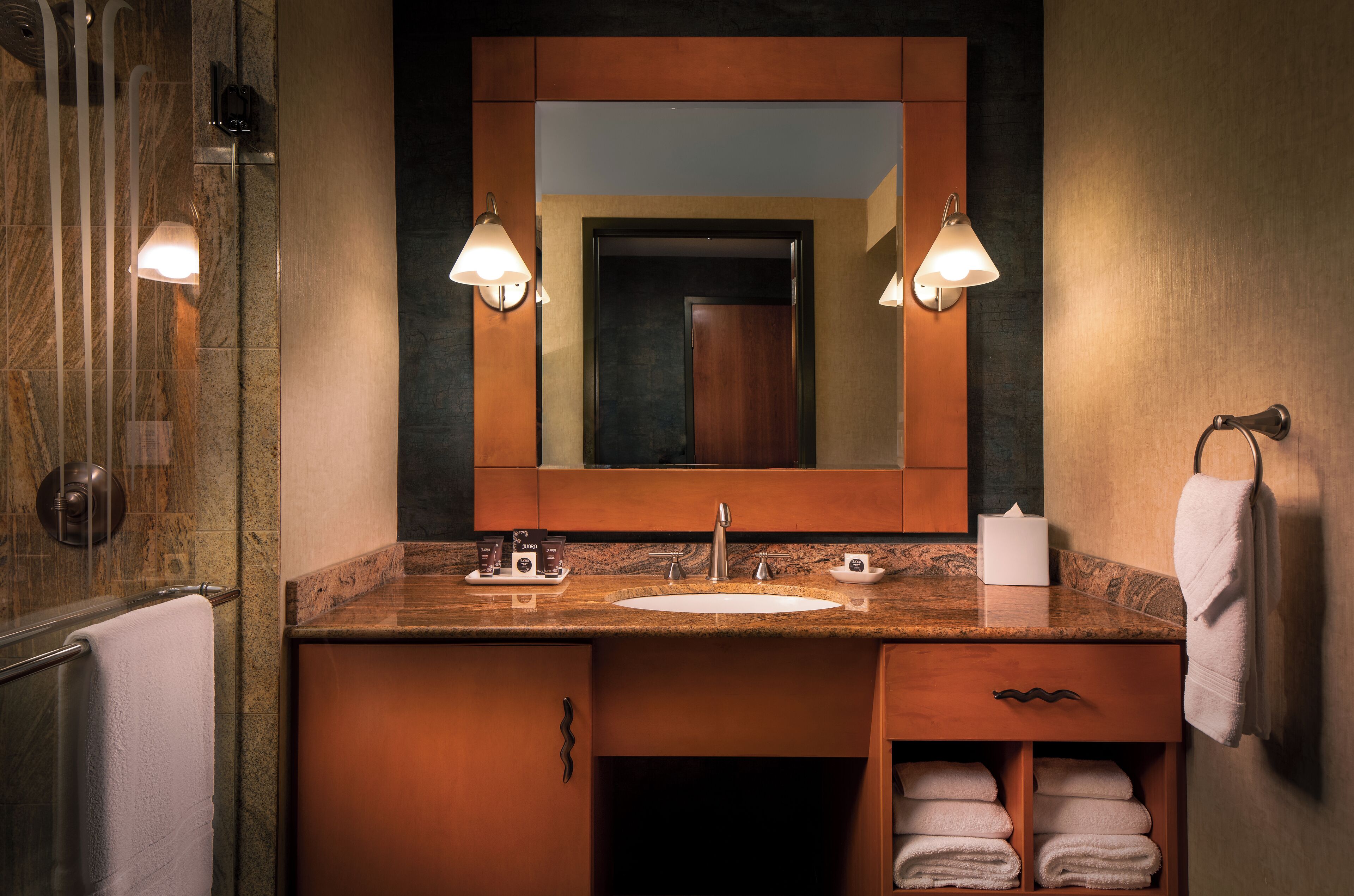 A bathroom with a marble countertop, a sink, a mirror, and two wall-mounted lights.